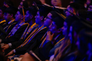 students sitting in a row wearing graduation caps and gowns